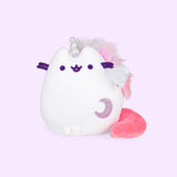 Super Pusheenicorn in a more triangular shape, resting her feet at the bottom and her plush pink tail sticking out to the side. Super Pusheenicorn has a unicorn horn in between her ears and a light purple sparkly crescent moon on the lower right of her front body. Her lilac and pink mane sticks out from behind her. There is a single white wing on her side.