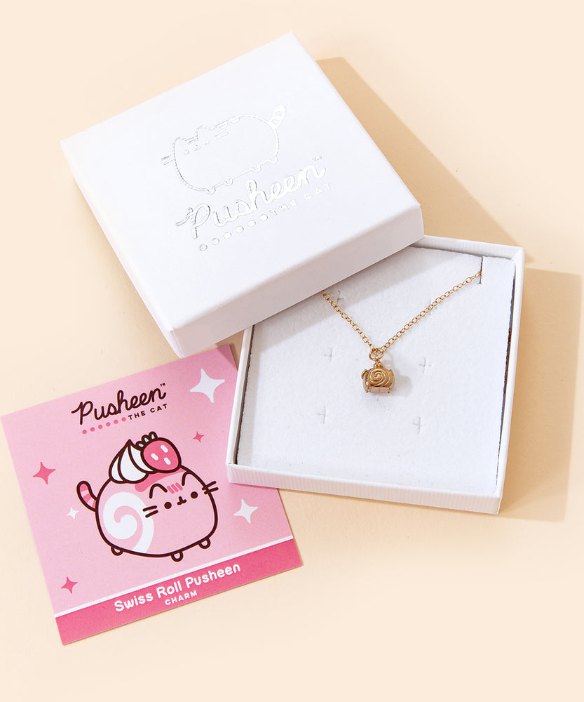 A small white square jewelry box with the lid removed and placed on the top left corner of the box holding the Gold Swiss Roll Pusheen Charm Necklace. To the left is a pink square card insert featuring an illustration of the Swiss Roll Pusheen. The jewelry lid features the Pusheen the Cat logo printed in silver.