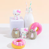 The four Squishy designs standing among pink donuts and a milk jug with two striped straws. The four possible surprise squishy designs include 2 designs of Hello Kitty sitting and 2 designs of Pusheen wearing Hello Kitty’s pink bow, with them either holding a milk jug with a straw or a mint donut.