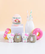 Four mini squishys lined up in front of pink donuts, a milk jug, and a small white podium holding up the egg shaped container the squishy arrive in. 