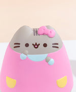Close up of the Pusheen Jumbo Squishy’s head in front of a pale yellow background. Pusheen’s face and head stripes are printed directly on the squishy while the bow, ears, arms, and dress details are sculpted in. A seam is visible at the top of Pusheen’s head.