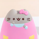 Close up of the Pusheen Jumbo Squishy’s head in front of a pale yellow background. Pusheen’s face and head stripes are printed directly on the squishy while the bow, ears, arms, and dress details are sculpted in. A seam is visible at the top of Pusheen’s head.