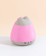 Back view of the Pusheen Jumbo Squishy facing to the left, seated on a white floor in front of a pale yellow background. There are no details on the back of Pusheen’s dress, and her striped tail rests sideways underneath her dress.
