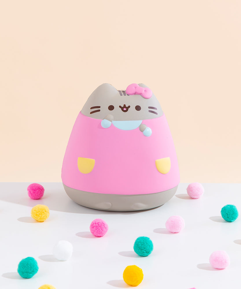Front view of the Pusheen Jumbo Squishy seated among pink, yellow and teal puff balls in front of a pale yellow background.