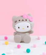 Front view of the Hello Kitty Jumbo Squishy seated on a white floor among pink, yellow and teal puff balls in front of a pink background.
