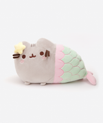 Quarter view of the Mermaid Pusheen Plush facing the left in a white space. The scale embroidery does not line up with the top seam of the plush, making the center scales look like a soft ‘W’ until it tapers down. The information tag for the plush is underneath the tail, by the plush pink fin.