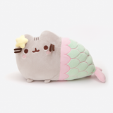 The Mermaid Pusheen Plush in a white space. The right side resembles the standard Pusheen with her feet on the floor, save for the embroidered pink cheeks underneath her eyes and the plush yellow star attached to her left ear. The mermaid tail starts halfway through the plush, with a pink scallop rim before the seafoam green tail with scale lines embroidered in pink. The tail tapers down to a plush pink fin that pokes out to the right.