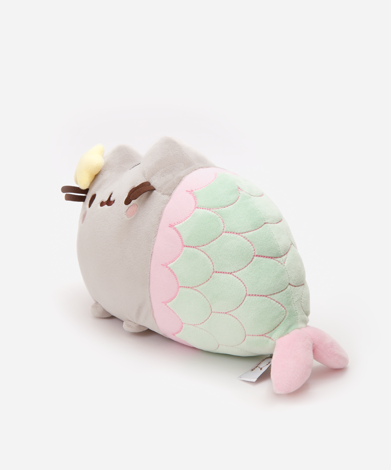 Quarter view of the Mermaid Pusheen Plush facing the left in a white space. The scale embroidery does not line up with the top seam of the plush, making the center scales look like a soft ‘W’ until it tapers down. The information tag for the plush is underneath the tail, by the plush pink fin.