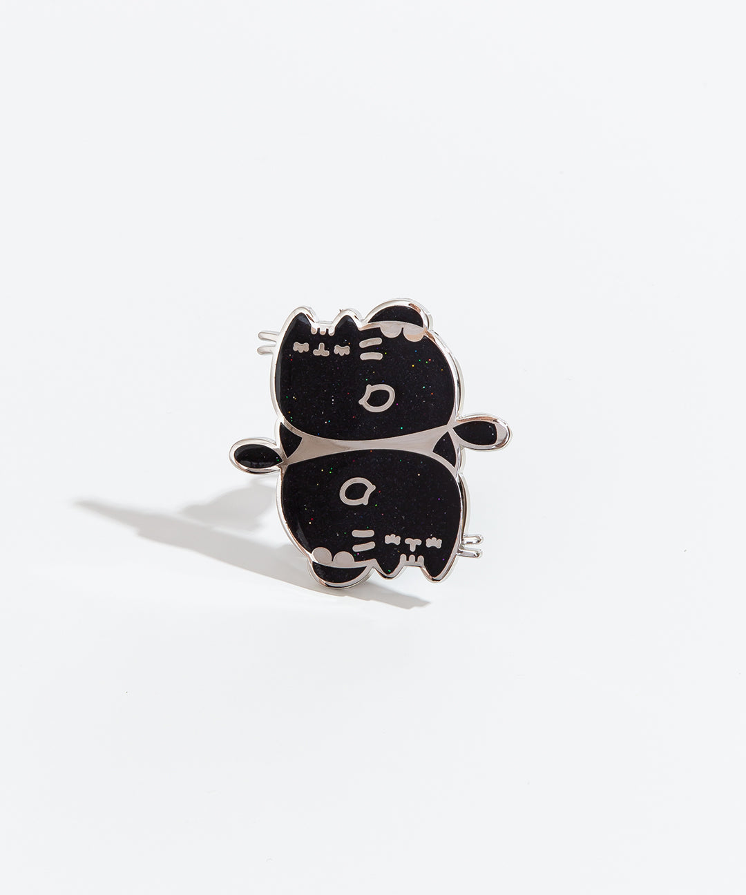 The Pisces pin on a white background. The pin feature two Pusheens with closed eyes and fish fins, mirroring each other vertically. The pin is black with multicolor sparkles and a silver outline.