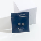 The back of the pin’s square paper packaging, leaning against a white square pedestal. The back is a solid navy blue with a white line near the top. The Chocking hazard warning and age range is noted at the top, the stoppers for the pin is located in the middle, and the copyright information is noted in white at the bottom.