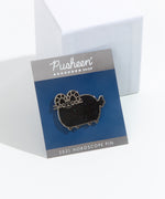 The Aries pin in its packaging, leaning against a white square pedestal. The square cardboard packing is a dark blue, with a grey banner on top displaying the Pusheen Shop logo and the banner at the bottom that reads ‘2021 Horoscope Pin’.